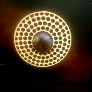 May include: A circular, gold-colored door knob with a raised, textured pattern of small circles. The knob has a dark brown center.