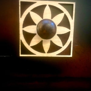 Może przedstawiać: Drewniany uchwyt do szuflady z okrągłym wzorem w kształcie gwiazdy. Uchwyt ma ciemnobrązowy metalowy gałkę w środku.