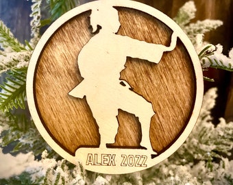 May include: A wooden Christmas bauble featuring a silhouette of a person in a karate pose. The bauble is brown with a wood grain pattern and has the text "ALEX 2022" on the bottom.