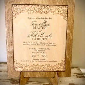 May include: A wooden wedding invitation with a laser-cut floral design. The invitation announces the wedding of Tara Allynn Mapes and Noah Alexander Gibson on Thursday, June 16, 2016 at 6:30 PM at The Lodge at Bridal Veil Falls, 2225 Bridal Veil, Spring Branch, Texas. The invitation includes a request to RSVP by May 2 at theknot.com/us/tara-and-noah.