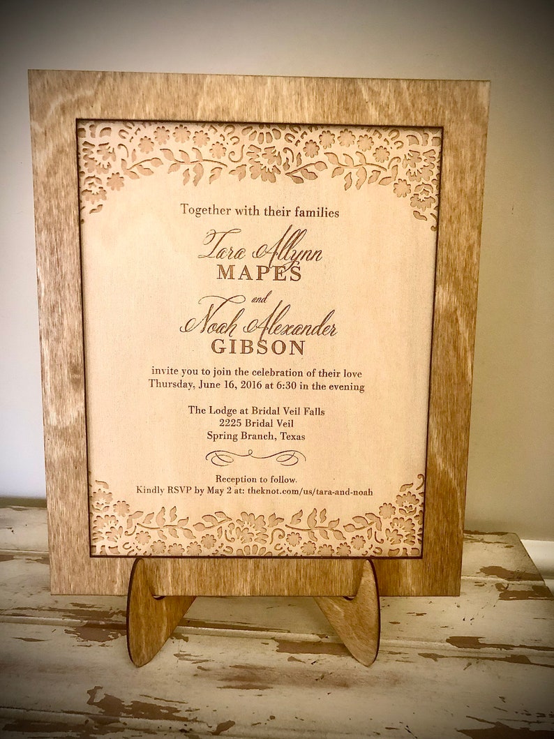 May include: A wooden wedding invitation with a laser-cut floral design. The invitation announces the wedding of Tara Allynn Mapes and Noah Alexander Gibson on Thursday, June 16, 2016 at 6:30 PM at The Lodge at Bridal Veil Falls, 2225 Bridal Veil, Spring Branch, Texas. The invitation includes a request to RSVP by May 2 at theknot.com/us/tara-and-noah.