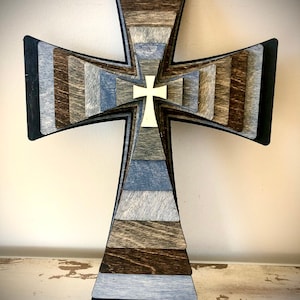 May include: A layered wooden cross with a white cross in the center. The cross is made of different shades of brown and blue wood.