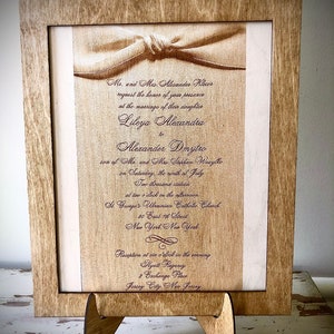 May include: A wedding invitation card with a brown wooden frame. The card is printed with a white background and brown text. The text reads: "Mr. and Mrs. Alexander Klecor request the honor of your presence at the marriage of their daughter Lileya Alexandra to Alexander Dmytro son of Mr. and Mrs. Stephan Wasylko on Saturday, the ninth of July Two thousand stateen at two o'clock in the afternoon St. George's Ukrainian Catholic Church 80 East 7th Street New York New York Reception at six o'clock in the evening Hyatt Regency 2 Exchange Place Jersey City, New Jersey"