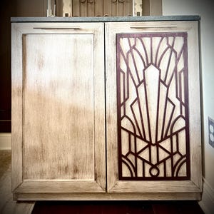 May include: A white wooden cabinet with two doors. The right door has a geometric design in a dark brown color.