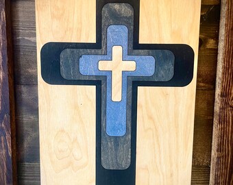 May include: A wooden cross with multiple layers of blue and black paint. The cross is on a light wood background.