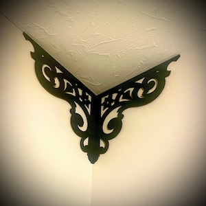 May include: Black decorative corner bracket with a detailed, intricate design. The bracket is made of wood and has a dark finish.