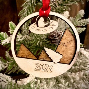Big Foot Yeti Sasquatch flying a UFO searching for Christmas tree 2-layer laser cut wood ornament, gift tag available unfinished or stained