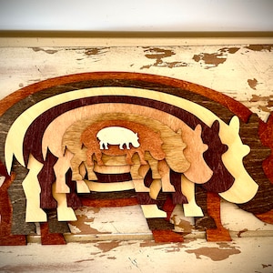 Pode incluir: Uma peça de arte de parede de madeira em camadas com a forma de um hipopótamo. O hipopótamo é feito de múltiplas camadas de madeira, cada uma de uma cor diferente, criando um efeito arco-íris. As camadas são cortadas na forma de um hipopótamo, com a camada menor no centro e a camada maior no exterior.