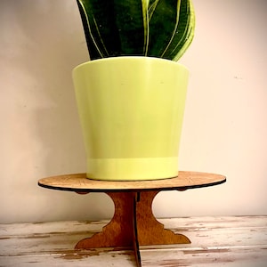 May include: A wooden plant stand with a round top and three legs. A potted plant with green and yellow leaves sits on the stand.