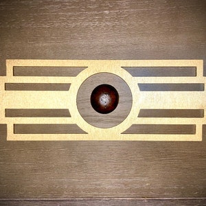 Puede incluir: Un diseño de metal dorado con un corte circular en el centro. El corte presenta una perilla redonda de color marrón oscuro.