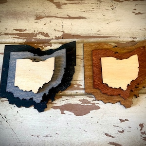 May include: Two wooden Ohio state outline shapes, one with a black and gray woodgrain finish and the other with a brown woodgrain finish.