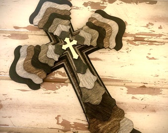 May include: A layered wooden cross with a gold-colored cross in the center. The cross is made of different shades of brown and gray wood.