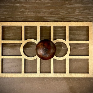 May include: A gold-colored metal grid with a brown sphere in the center. The grid has a square shape with a decorative pattern of circles.