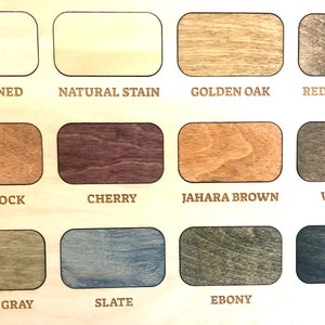 May include: A wood stain color chart featuring twelve rectangular samples arranged in three rows. Each sample displays a unique wood grain finish labeled with text: Unstained, Natural Stain, Golden Oak, Red Chestnut, Gunstock, Cherry, Jahara Brown, Walnut, Smoke Gray, Slate, Ebony, and Black.