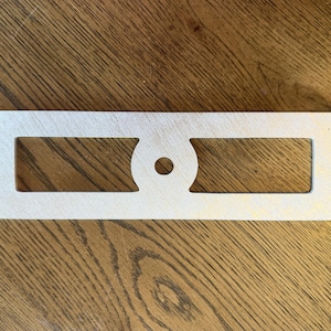 May include: A rectangular silver-colored metal plate featuring a brushed finish. The plate has two elongated rectangular cutouts separated by a central circular section containing a single small hole in the middle for mounting or attachment purposes.