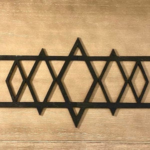 Könnte beinhalten: Schwarze Wanddekoration aus Metall mit geometrischem Design, das aus einer Reihe ineinandergreifender Diamanten und Sterne besteht. Die Dekoration hat zwei runde Knöpfe auf jeder Seite.