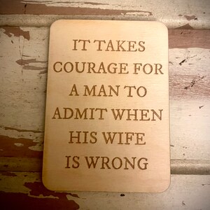 May include: Wooden sign with the text "It takes courage for a man to admit when his wife is wrong."