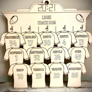 May include: A wooden sign with a scoreboard design featuring the word "LIONS" and "COACH DOM" with a football jersey for each player on the team. The jerseys have numbers from 1 to 88.