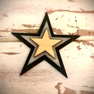May include: A wooden star with three layers, the top layer is a light brown color, the middle layer is a dark blue color, and the bottom layer is a black color.