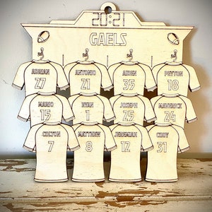 May include: A wooden sign with the word "GAELS" and a scoreboard that reads "20:21". The sign has a design of 12 jerseys with names and numbers on them. The jerseys are in a light wood color.