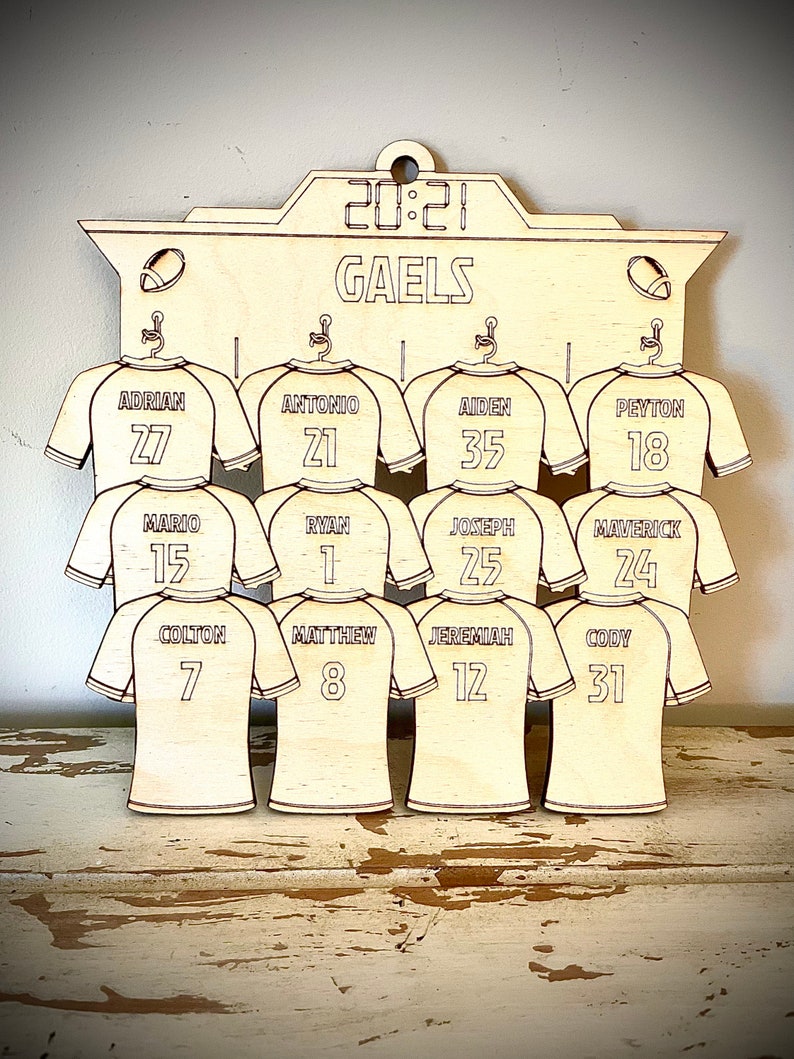 May include: A wooden sign with the word "GAELS" and a scoreboard that reads "20:21". The sign has a design of 12 jerseys with names and numbers on them. The jerseys are in a light wood color.