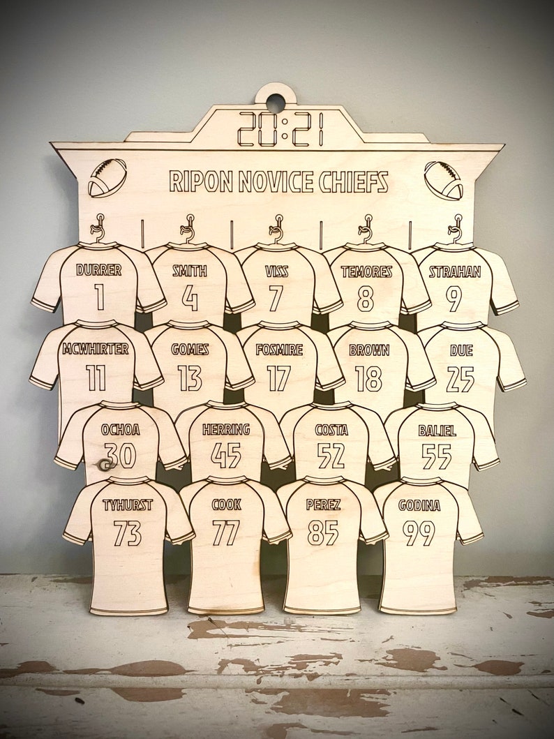 May include: A wooden sign with a scoreboard design featuring the text "RIPON NOVICE CHIEFS" and a list of names and numbers. The sign is decorated with football jerseys and footballs.