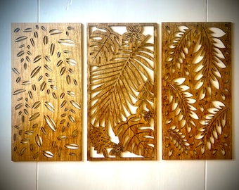 May include: Three wooden wall decor panels with a tropical leaf design. The panels are stained a light brown color and have a cutout design of leaves and flowers.