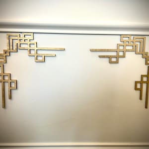 May include: Two gold geometric corner moldings on a white wall. The moldings are made of wood and have a simple, modern design.