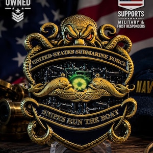 May include: A gold and black metal challenge coin featuring a kraken at the top, the text UNITED STATES SUBMARINE FORCE, a central green glowing emblem, two gold dolphins, and the text SNIPES RUN THE BOAT at the bottom of the shield-shaped design.