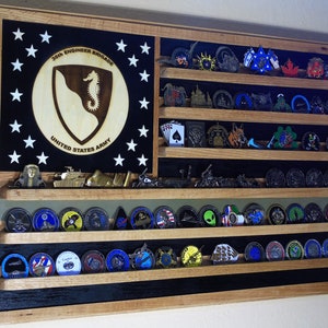 May include: A wooden shadow box with a black background and a US flag design. The shadow box has multiple shelves for displaying challenge coins. The top shelf features a round emblem with the text "36th Engineer Brigade United States Army".