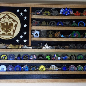 May include: A wooden shadow box with a black and white American flag design. The shadow box has six shelves with rows of military challenge coins. The top shelf has a round wooden plaque with the text "502nd Engineer Brigade United States Army".