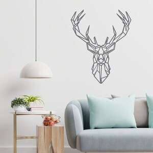 May include: A geometric deer head wall decal in gray, a light gray sofa with a light blue throw pillow, a wooden side table with a bowl of red apples, and a white pendant light hanging from the ceiling.