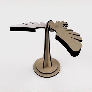 May include: A wooden bird sculpture with a beige body and black edges. The bird has outstretched wings and is mounted on a beige stand with a circular base. The sculpture is a decorative item.