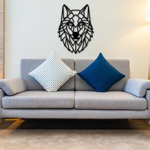 Könnte beinhalten: Ein graues Sofa mit zwei Kissen, eines weiß mit einem Streifenmuster und eines blau. Ein schwarzer geometrischer Wolfskopf ist an der Wand über dem Sofa angebracht.