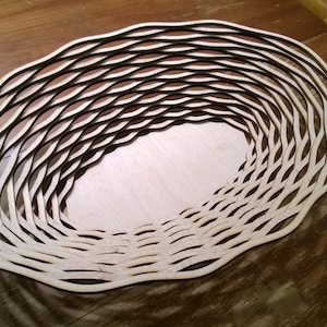 May include: A wooden bowl made of thin, interwoven strips of wood. The bowl is oval shaped and has a natural wood finish.