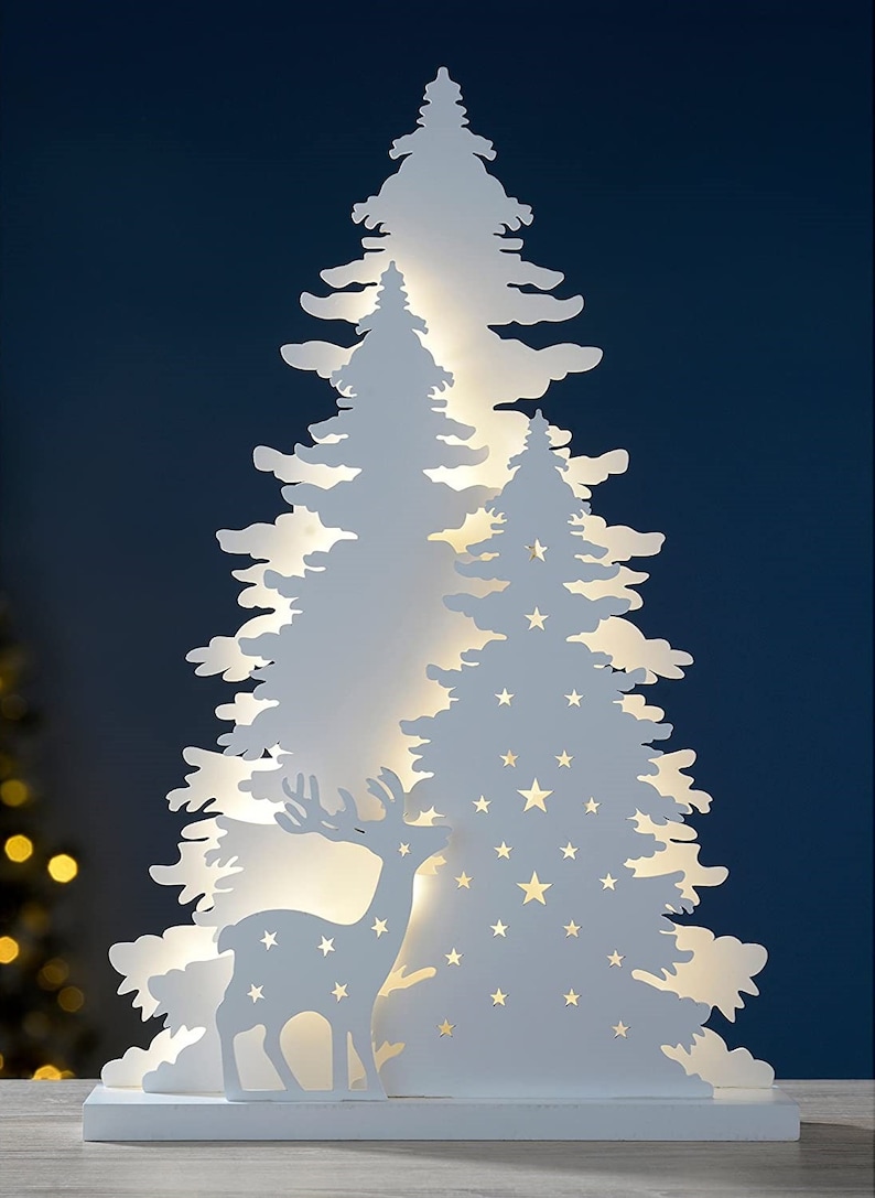 May include: White wooden Christmas tree silhouette with a deer and stars cut out. The tree is illuminated with warm white LED lights.