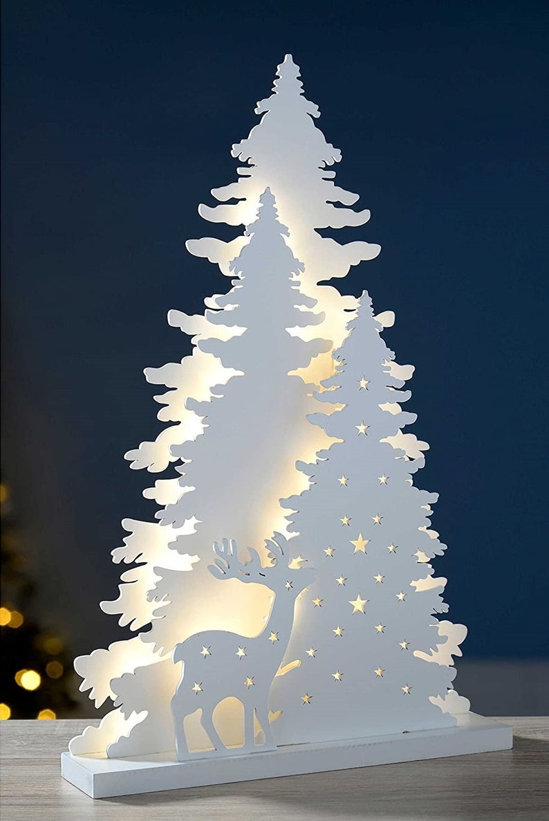 May include: White wooden Christmas tree silhouette with a deer and stars cut out. The tree is illuminated with warm white LED lights.