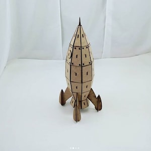 Könnte beinhalten: Ein hölzernes Raketenmodell mit brauner Oberfläche. Die Rakete hat eine spitze Nasenspitze und drei Flügel. Das Modell besteht aus vielen kleinen Teilen, die zusammengefügt werden.