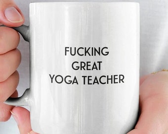Puede incluir: Taza de café de cerámica blanca con texto negro que dice "FUCKING GREAT YOGA TEACHER".