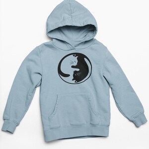 May include: A light blue hoodie with a black and white Yin Yang cat design. The hoodie features a hood, a front pocket, and long sleeves. The cat design is in a circular shape.
