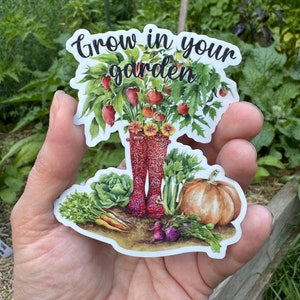 May include: A white sticker with a watercolor illustration of a pair of red rain boots filled with vegetables and flowers. The text "Grow in your garden" is written in black cursive above the boots.