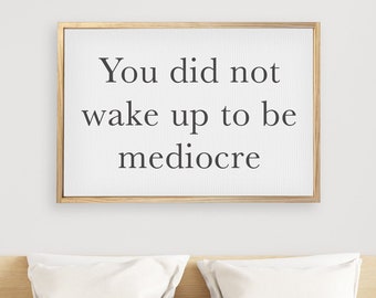 May include: A framed motivational quote on a white wall above a bed with white bedding. The quote reads "You did not wake up to be mediocre."