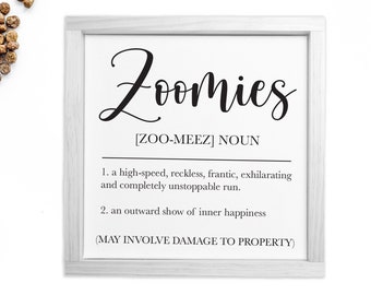 May include: A white framed print with the word "Zoomies" in black cursive lettering. The definition of the word is provided below in black text: "[ZOO-MEEZ] NOUN 1. a high-speed, reckless, frantic, exhilarating and completely unstoppable run. 2. an outward show of inner happiness (MAY INVOLVE DAMAGE TO PROPERTY)"