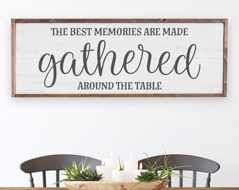 May include: A white wooden sign with a brown wood frame. The sign says "The best memories are made gathered around the table".