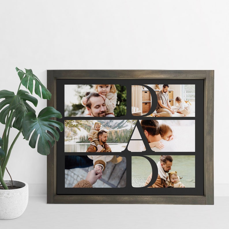 Op de afbeelding: Een ingelijste fotocollage met het woord "DAD" uitgesneden, met familiefoto's. De lijst is donkergrijs en de foto's tonen een vader met zijn kind. De collage wordt weergegeven op een witte achtergrond.