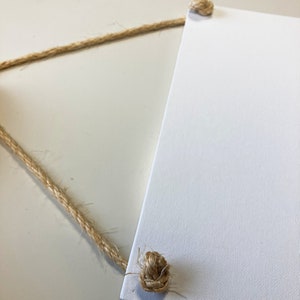 May include: A white canvas sign with two knots of natural twine attached to the top corners.
