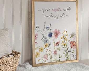 Puede incluir: Una impresión enmarcada con un diseño floral de acuarela con flores rosas, azules y amarillas. El texto "your custom quote in this font" está escrito en una fuente cursiva en la parte superior de la impresión.