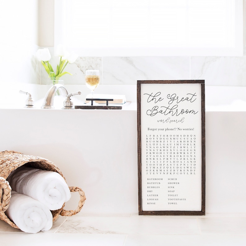 A framed 12x24 in Tobacco sits against a bathtub. "The Great Bathroom word search" is written at the top of the canvas with a bathroom-themed word search below.