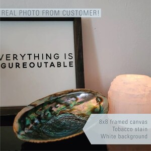 May include: An 8x8 inch framed canvas with the text "EVERYTHING IS FIGUREOUTABLE" in black lettering on a white background. The canvas is framed in a dark wood frame. The canvas is sitting on a table with a seashell and a white candle.