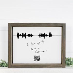Peut inclure: Impression sur toile encadrée dans un cadre en bois marron foncé. L'impression présente un motif d'onde sonore noir au-dessus d'un texte manuscrit qui dit "I love you!!!" et "xoxoxo Gretchen". Un code QR est en bas.